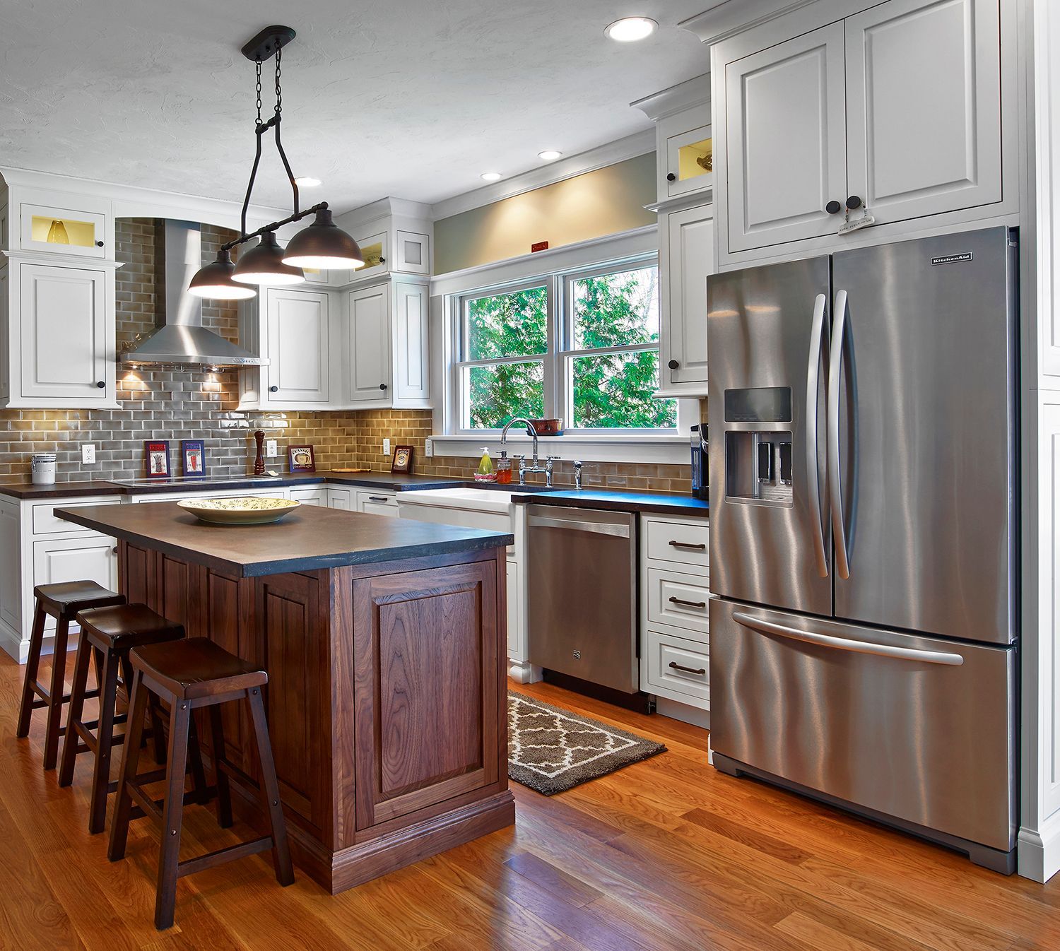 Bright modern kitchen with a dark island, stainless steel appliances, and wooden floors
