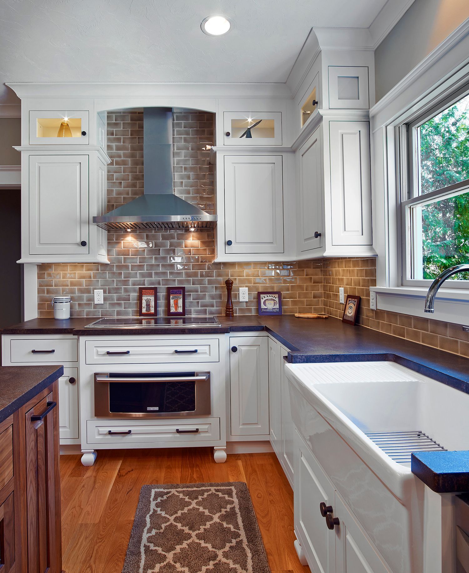 Bright white kitchen with stainless hood, brick backsplash, wood floor, and a large window over the sink
