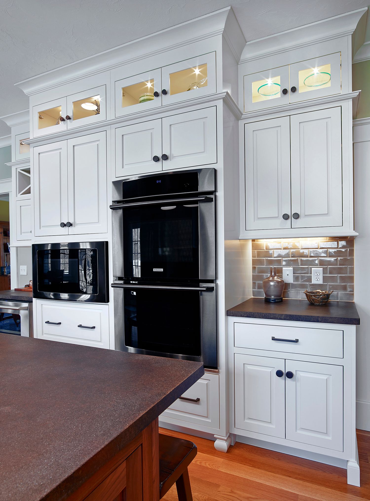 White kitchen with black appliances, dark countertops, and decorative glass cabinets.