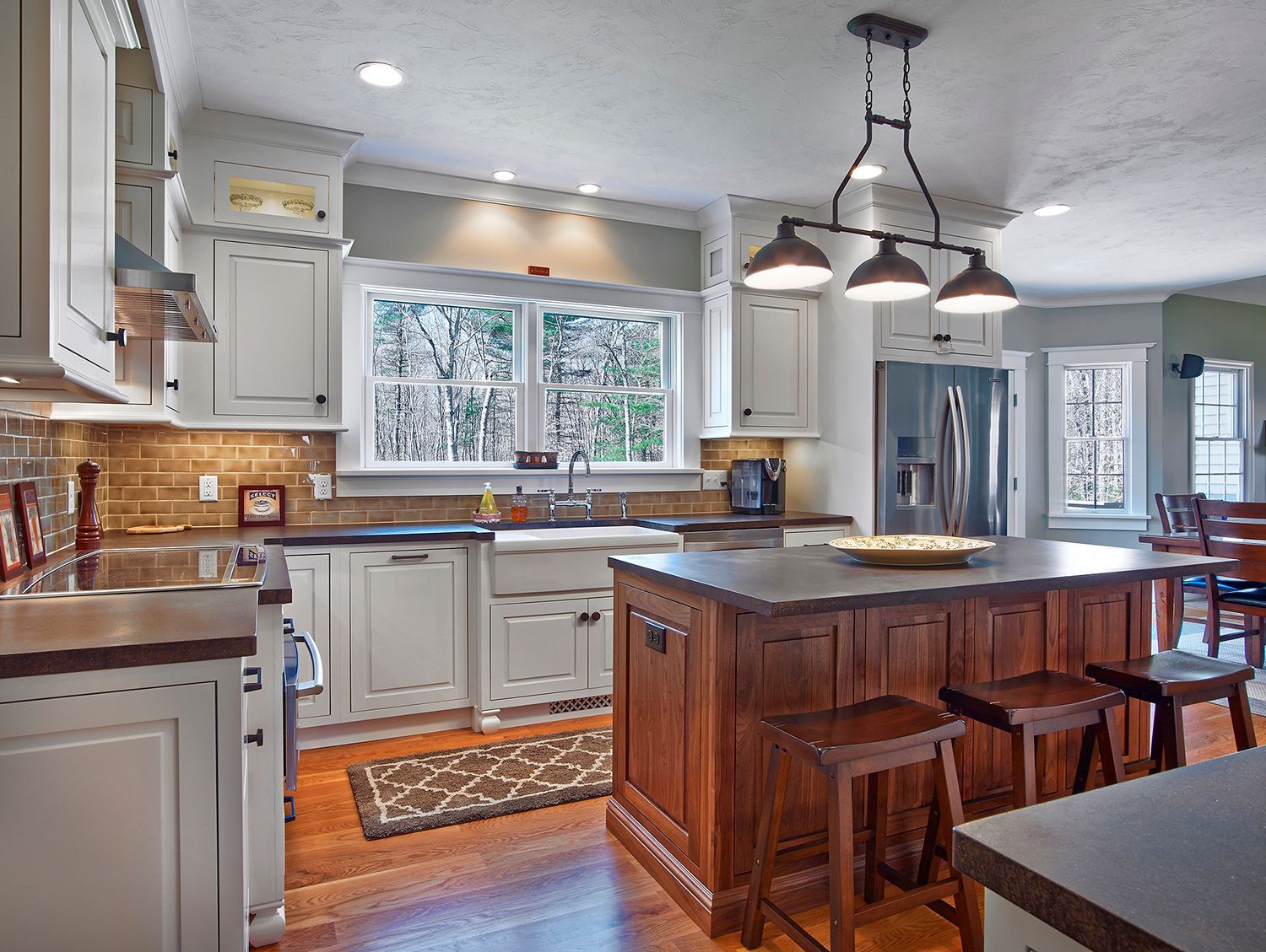 Bright kitchen with white cabinets, wood island, bar stools, and a large window over the sink.