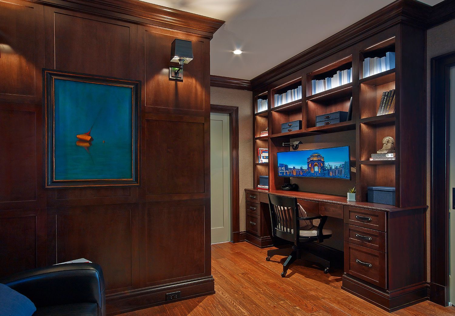 Wood-paneled home office with built-in desk, shelves, computer, and a blue accent window.
