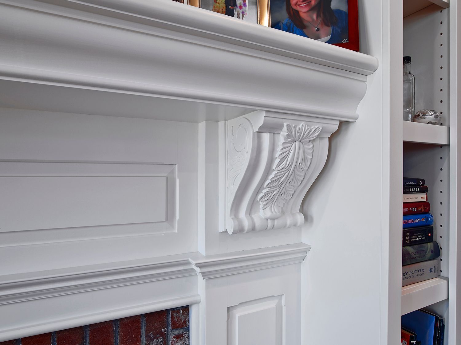 White ornate fireplace mantel with decorative molding and a nearby bookshelf