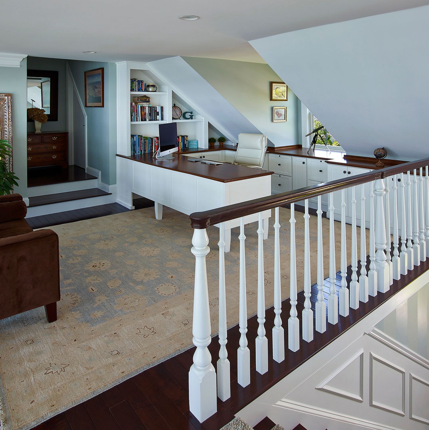 Bright living room with beige carpet, white railings, and a sloped ceiling over a stair landing.