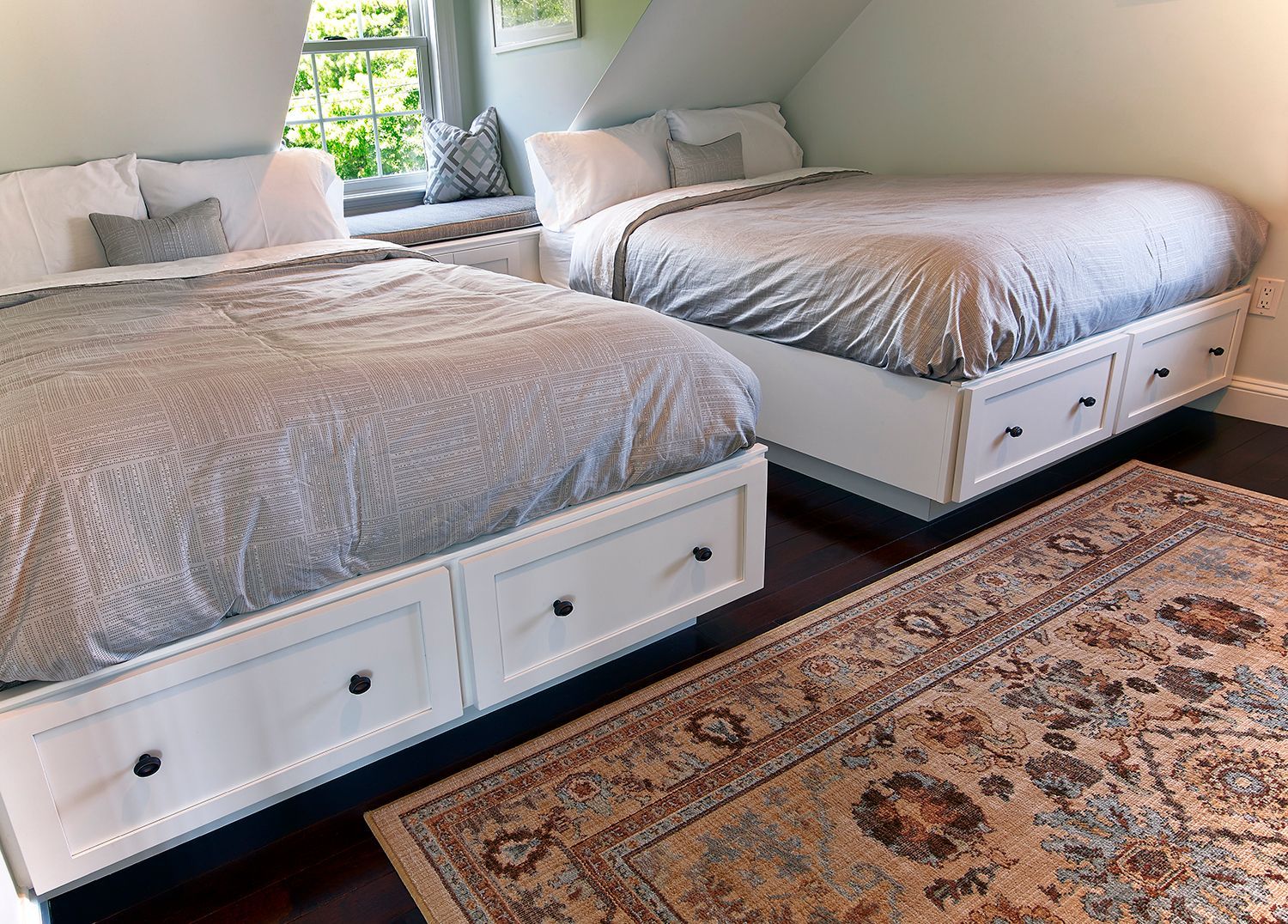 Two white beds with gray bedding in a bright bedroom beside a patterned rug