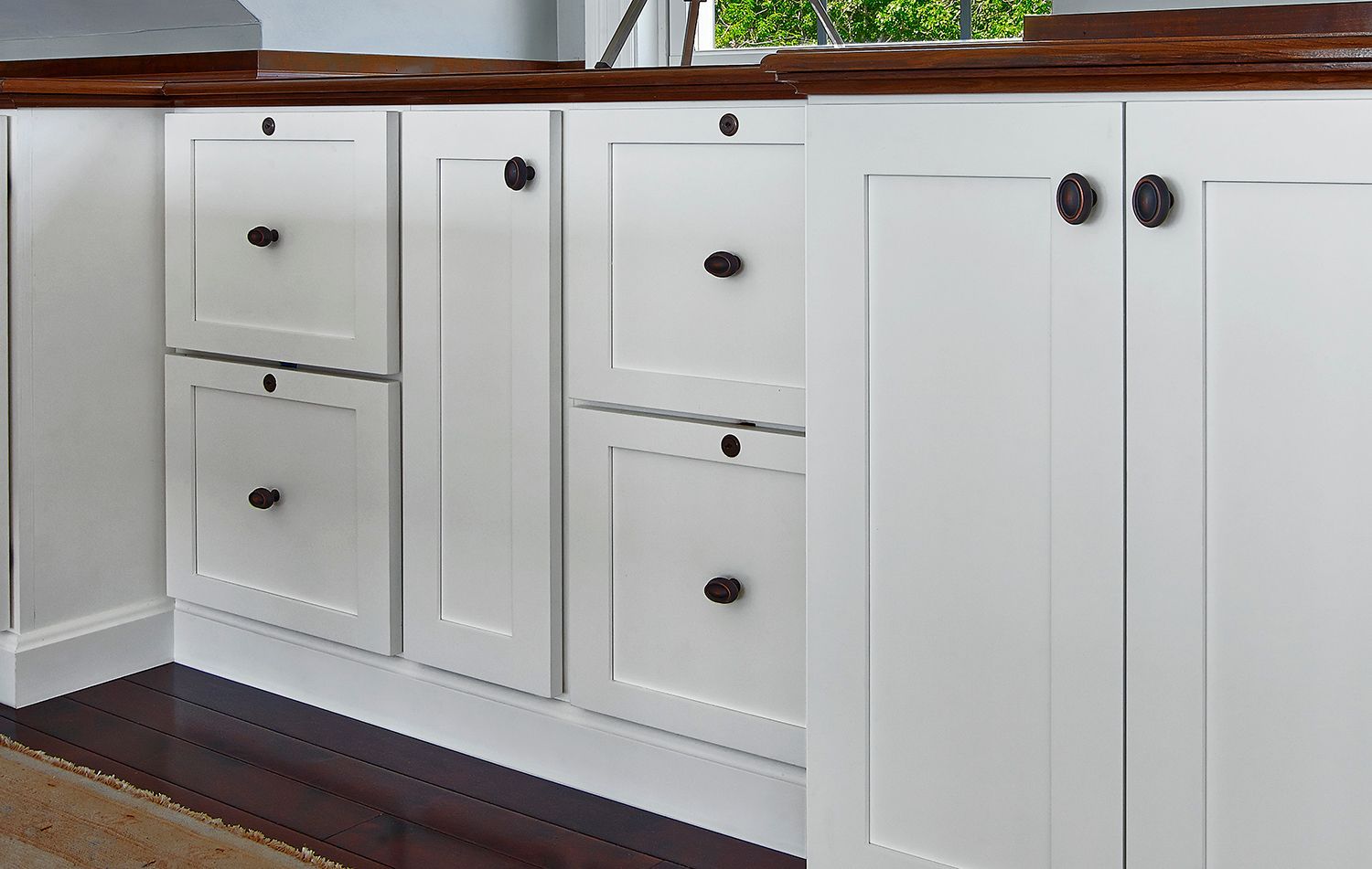 White kitchen cabinets with dark round knobs beneath a wooden countertop