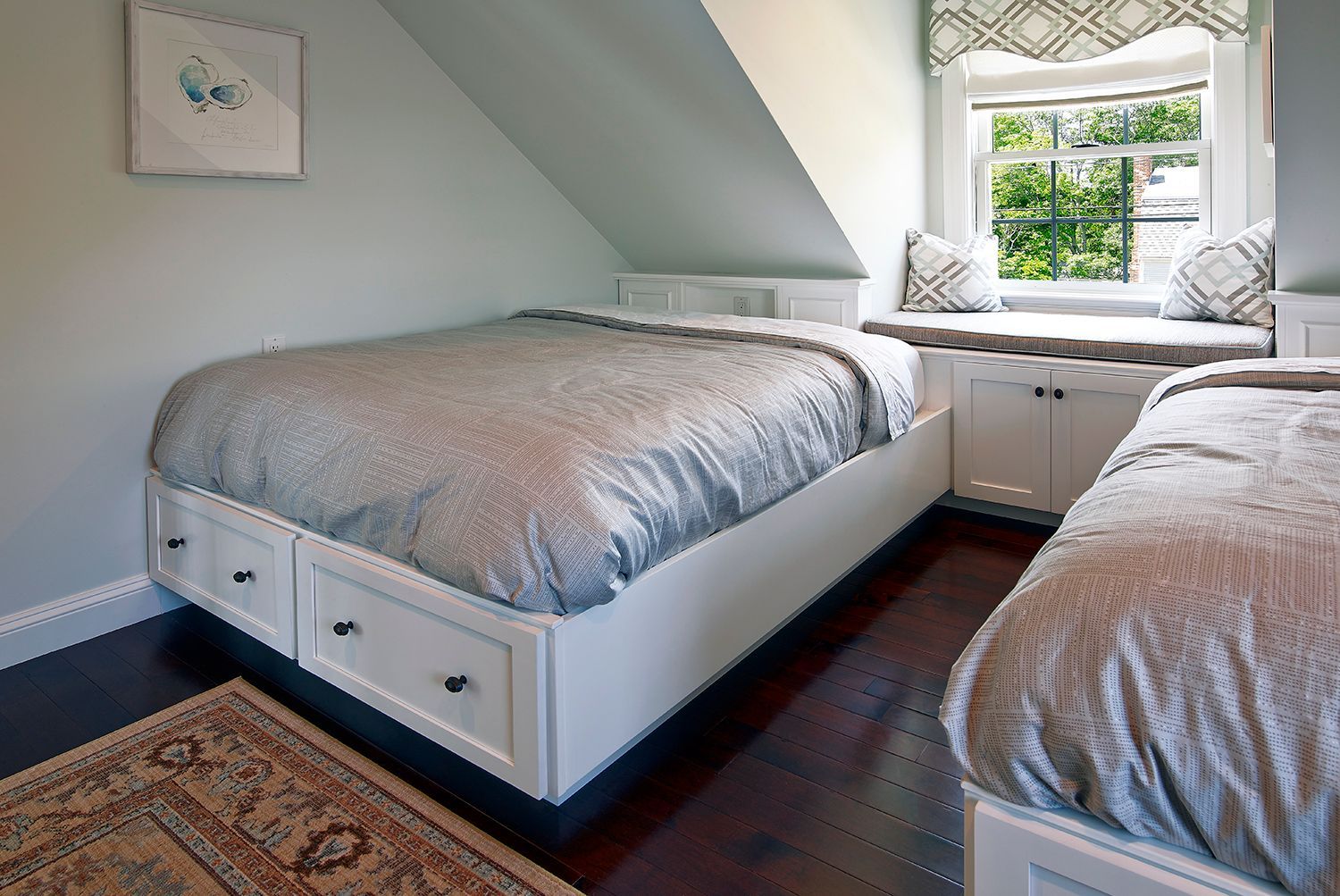 Small attic bedroom with two beds, white walls, and a window seat by the window.