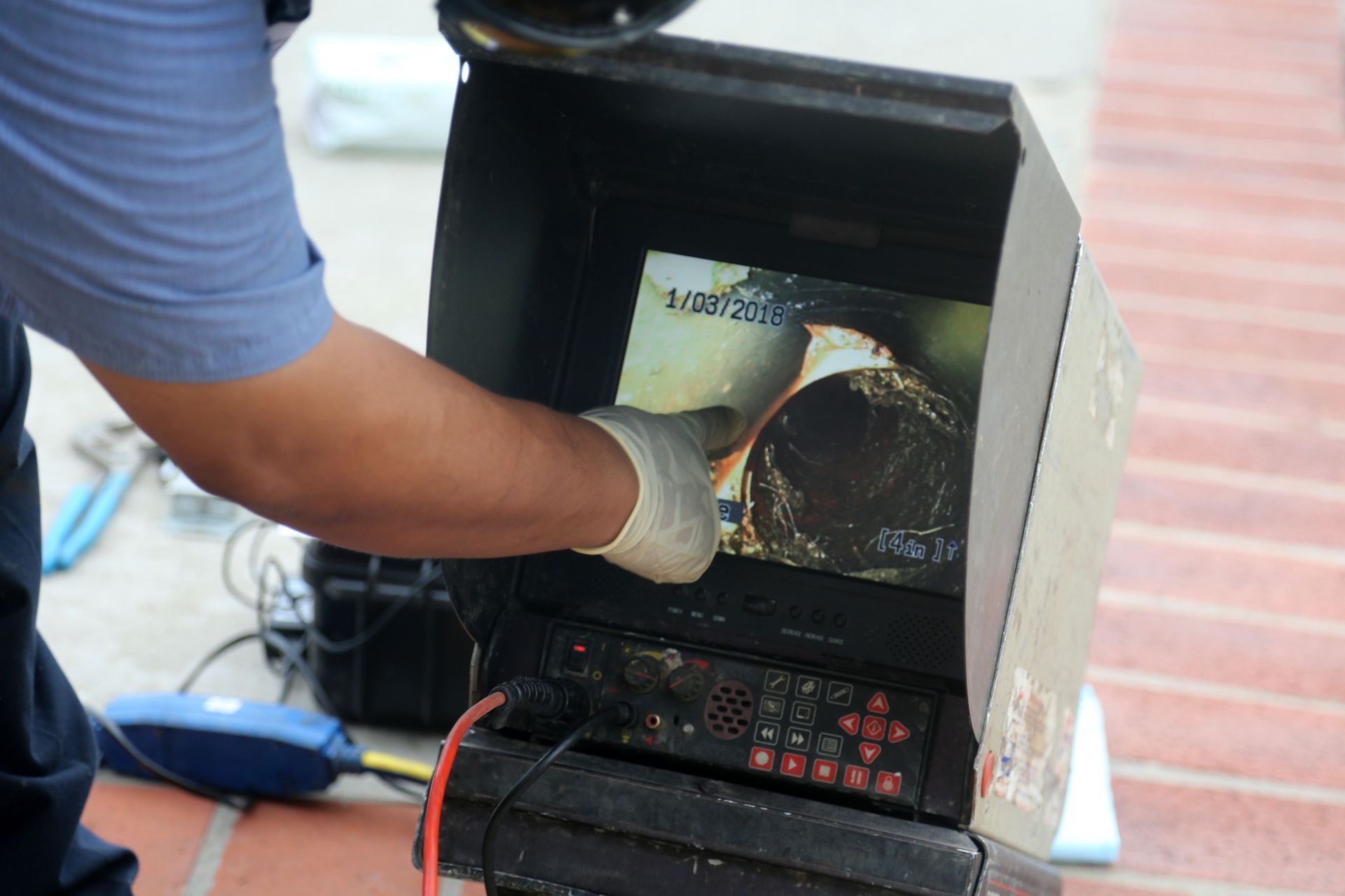 A person in a uniform pointing to a screen showing the inside of a pipe using a camera inspection tool.