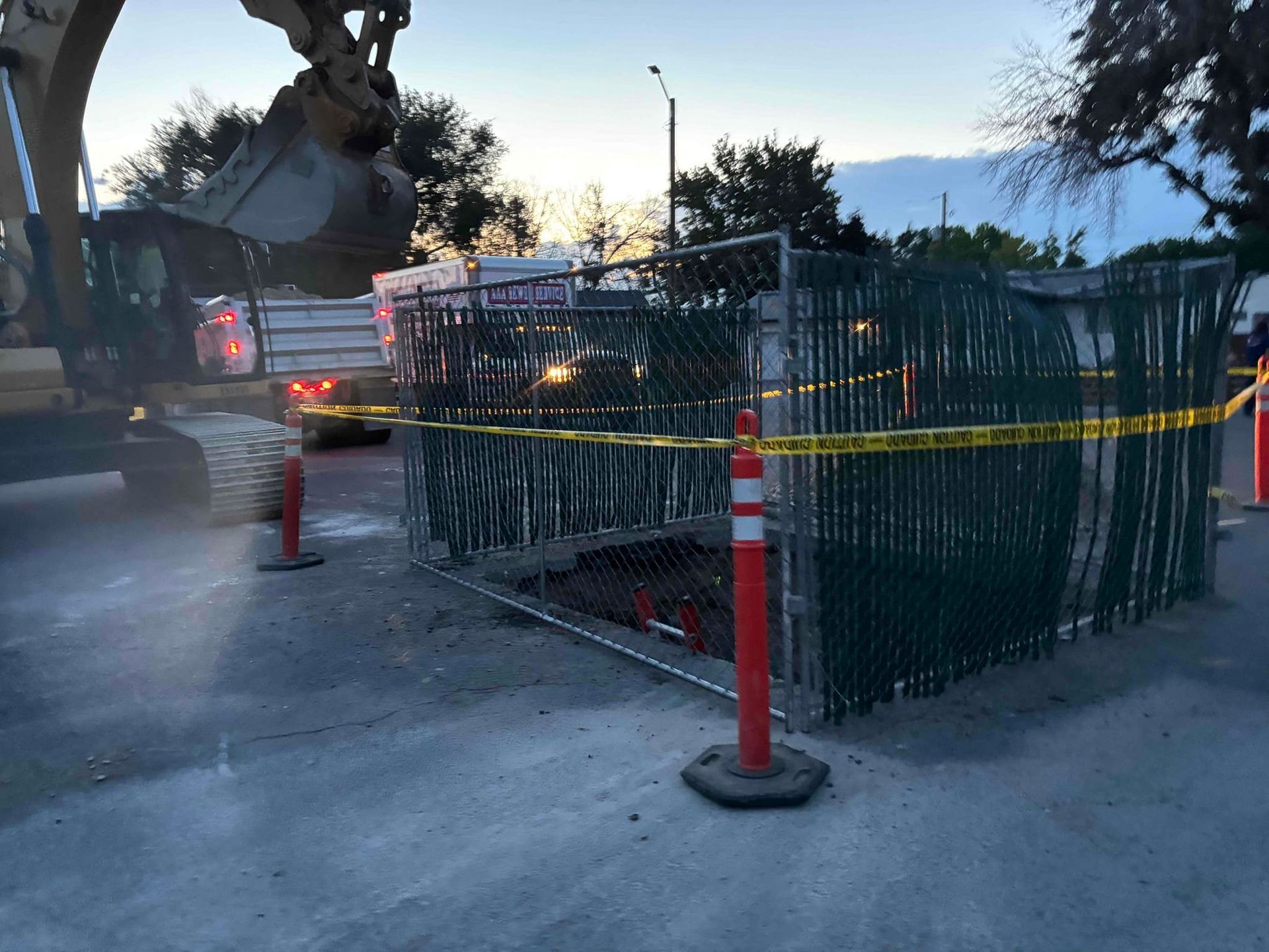 Excavator working on a construction site fenced off with caution tape and a green barrier in a parking lot.