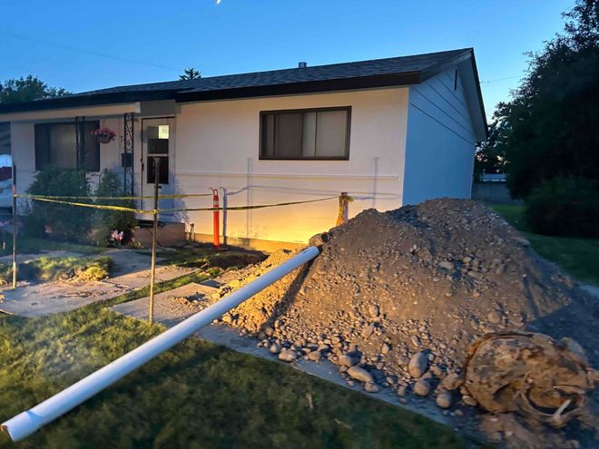 House with construction. Pile of dirt, white pipe, caution tape, and a dim, evening setting.