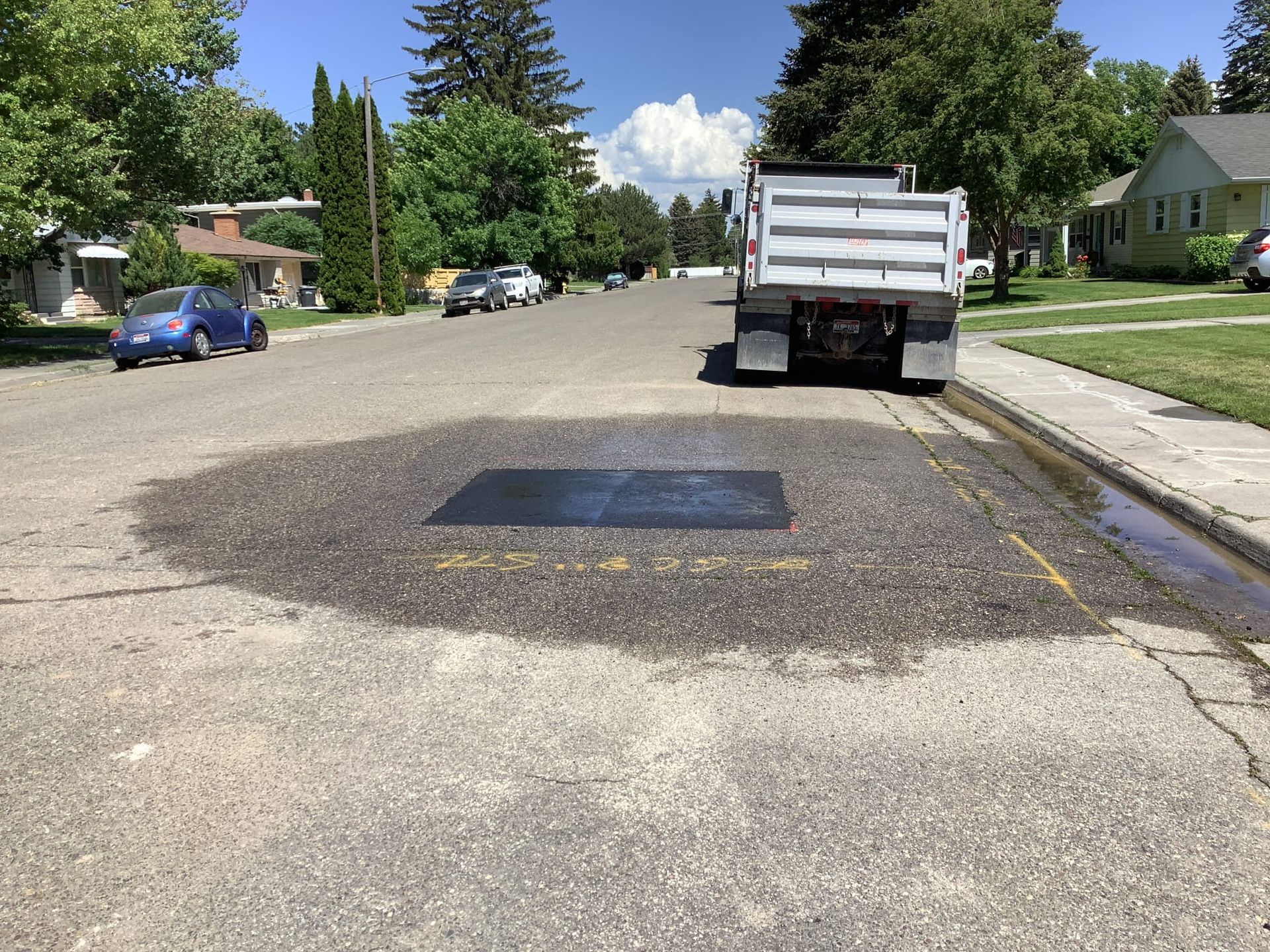 Road repair in progress: a dump truck spreads gravel over a patched section of street, residential area.