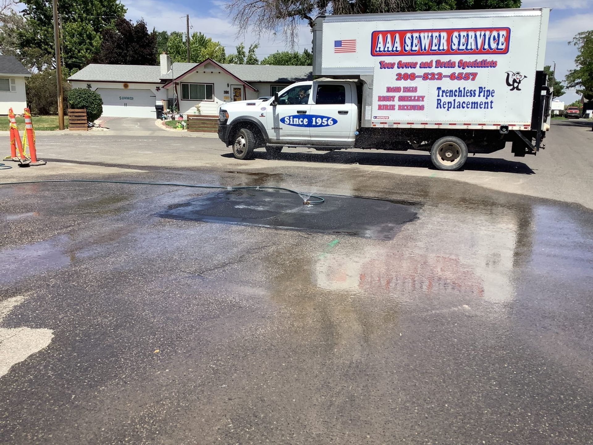 AAA Sewer Service truck parked on a street with a water leak; orange cones nearby.