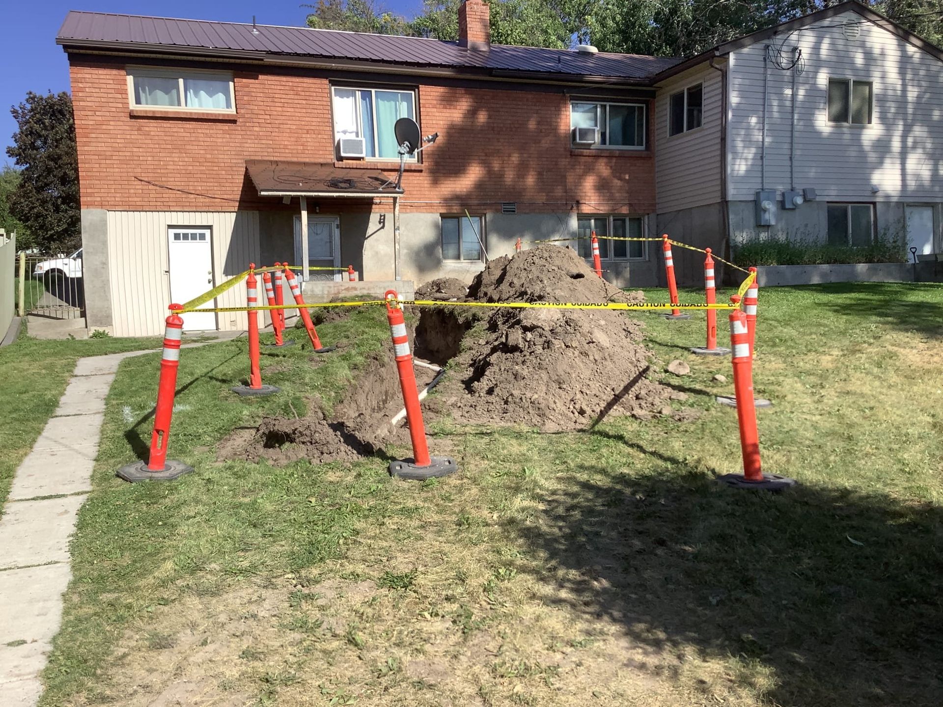 A pile of dirt surrounded by safety cones and tape in front of a brick building.