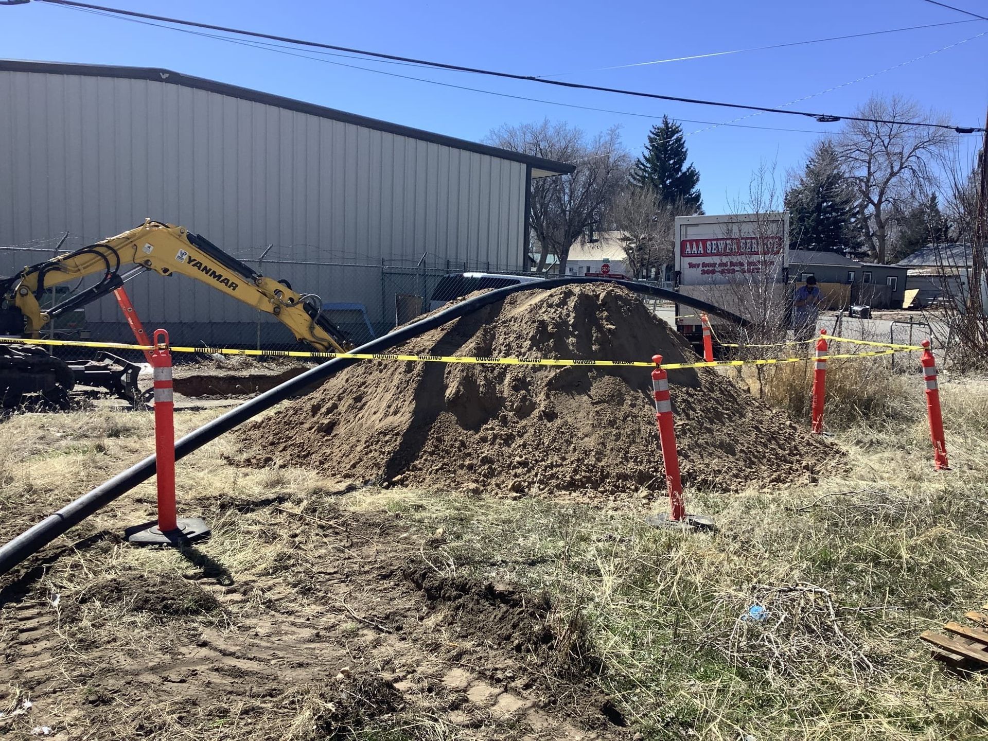 Construction site with a pile of dirt, a backhoe, and yellow tape.
