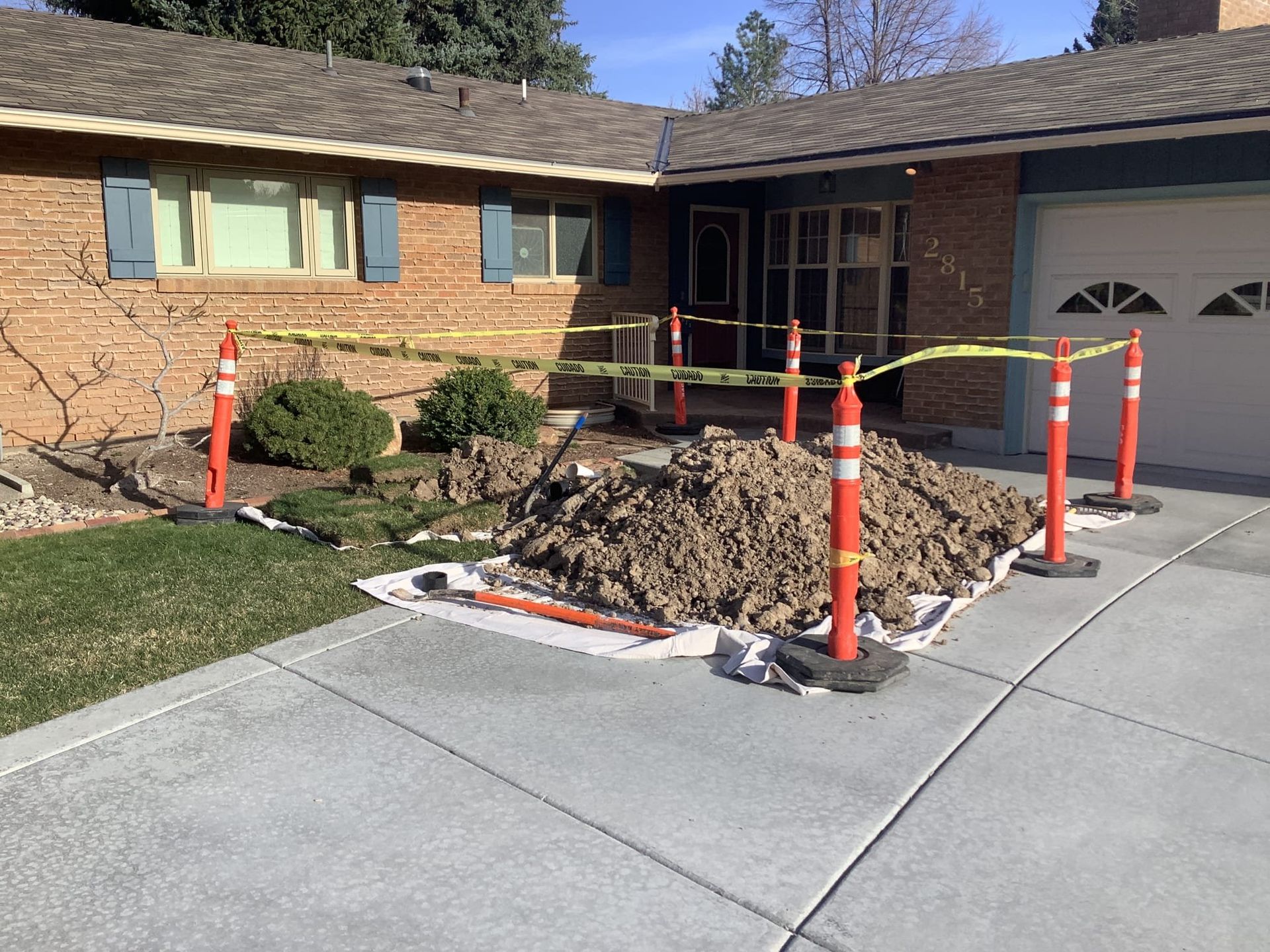 Exterior home with excavation site, orange posts, caution tape, and a pile of dirt on the driveway.