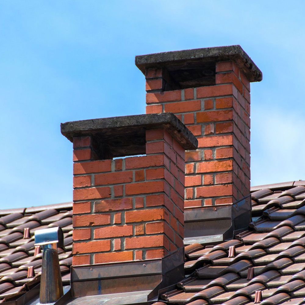 Two brick chimneys on a brown-tiled roof against a clear blue sky.