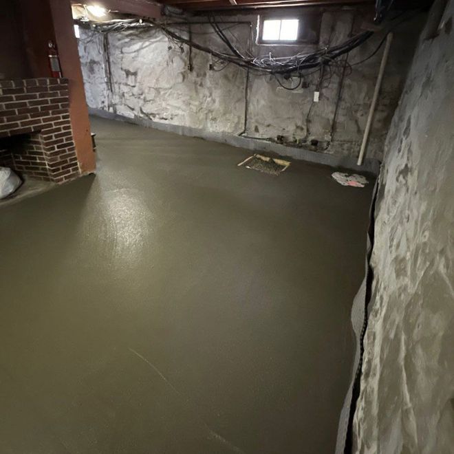 Basement with a smooth, wet concrete floor, brick fireplace, and stone walls.