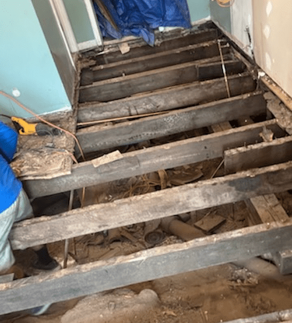 Staircase renovation: exposed wooden beams and debris, light blue wall, person working on stairs.