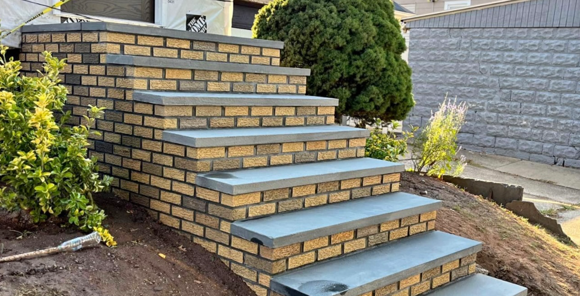 Brick steps with gray stone treads, surrounded by greenery and landscaping.