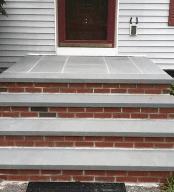 Brick and gray stone steps leading up to a red-framed door.