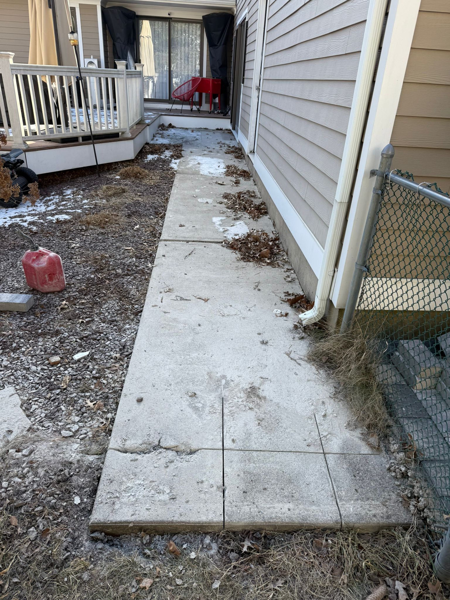 Concrete pathway next to a building and deck, covered in leaves and some snow.