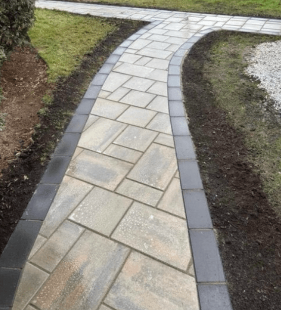 A paved path with a dark border curves through a green lawn, with a split path ahead.