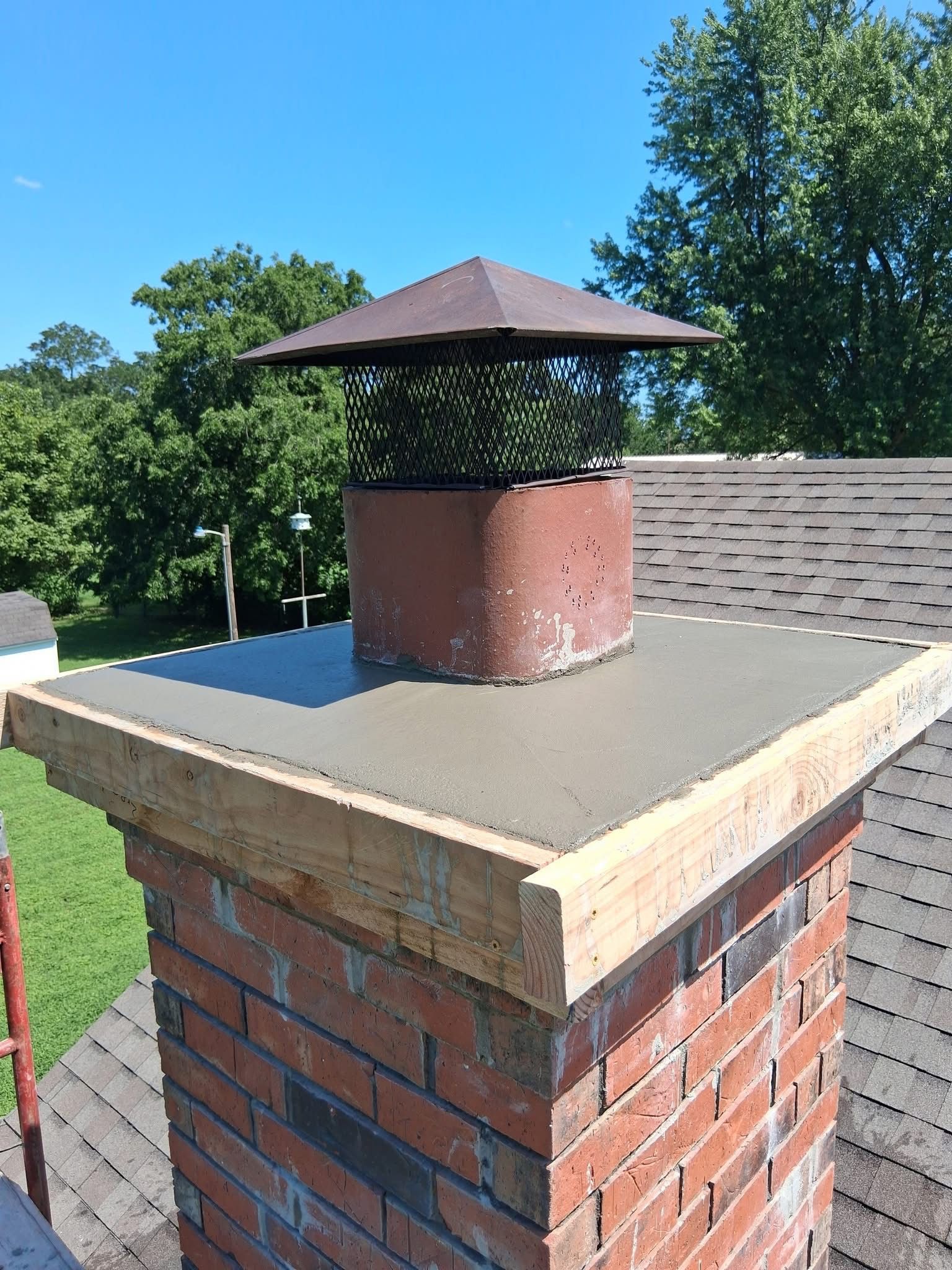 Brick chimney with a new concrete cap and chimney cap.