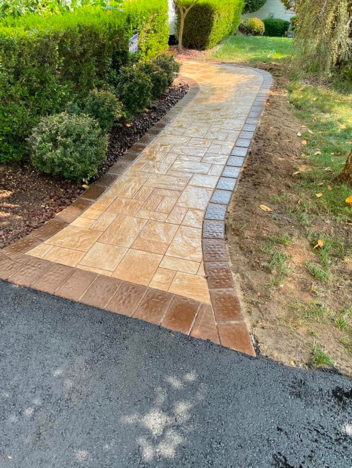 Brick pathway with brown border, leading from asphalt to a green yard.