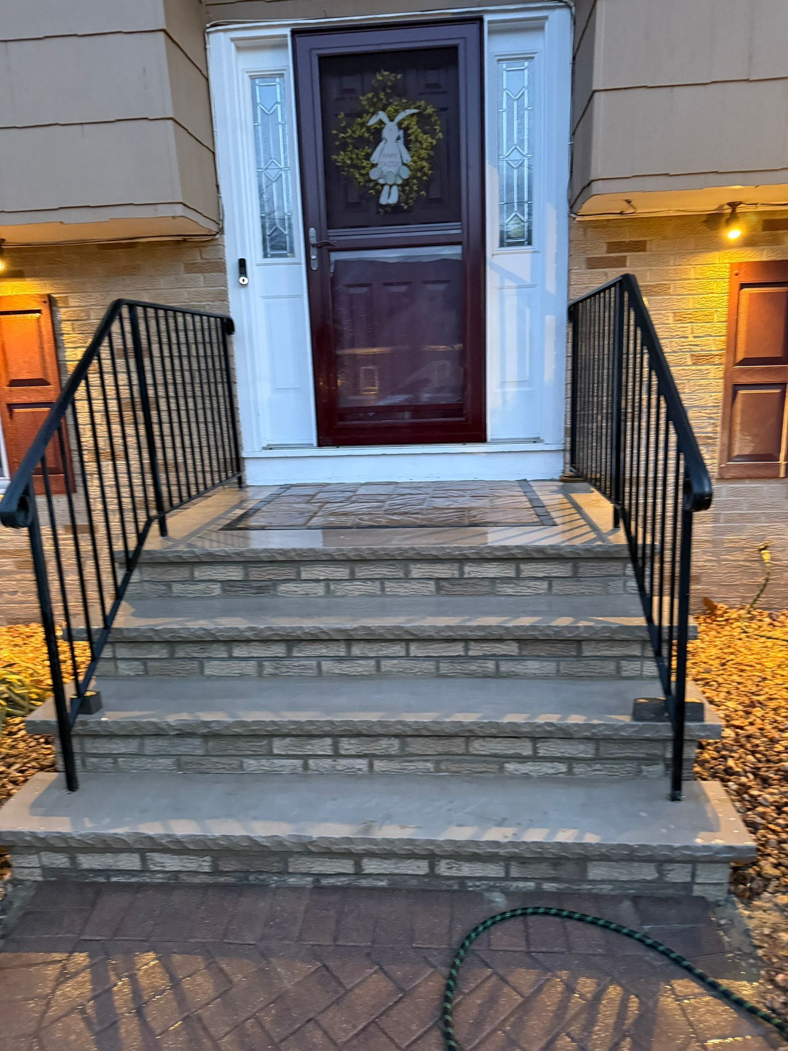 Brick steps leading to a front door with a wreath, black railings, and a doormat.