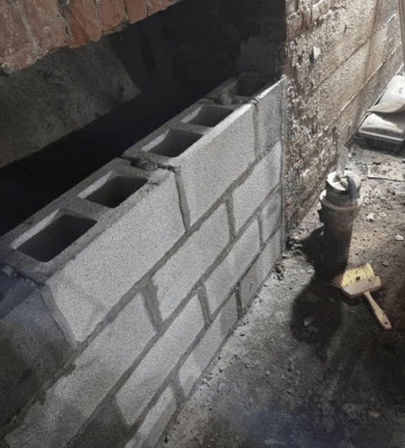 A partially built cinder block wall in a dark, unfinished basement.