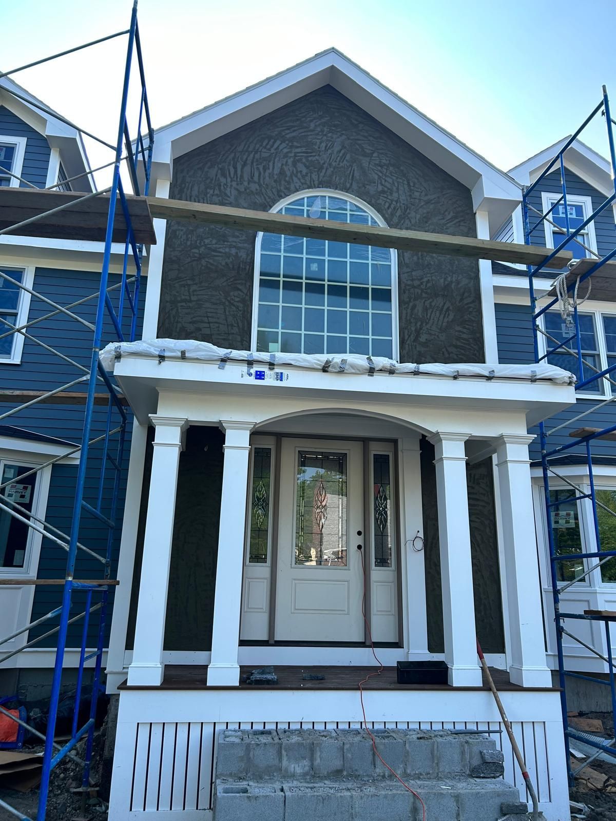 House exterior under construction with blue siding, white trim, porch, and scaffolding.
