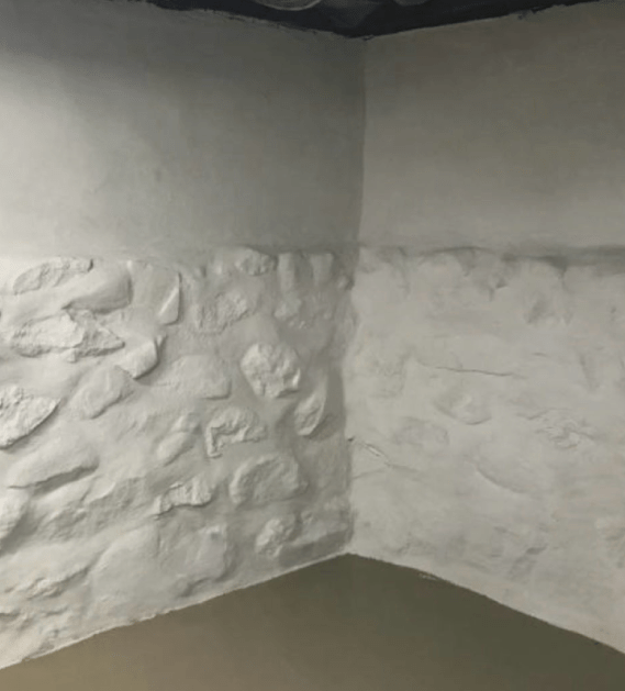 White-painted stone wall corner in a room. The wall is divided into a rock-like lower half and a smooth upper half.