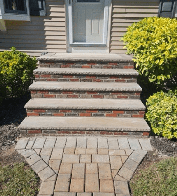 Brick steps leading to a cream-colored door, with brick walkway. Green bushes flank the stairs.