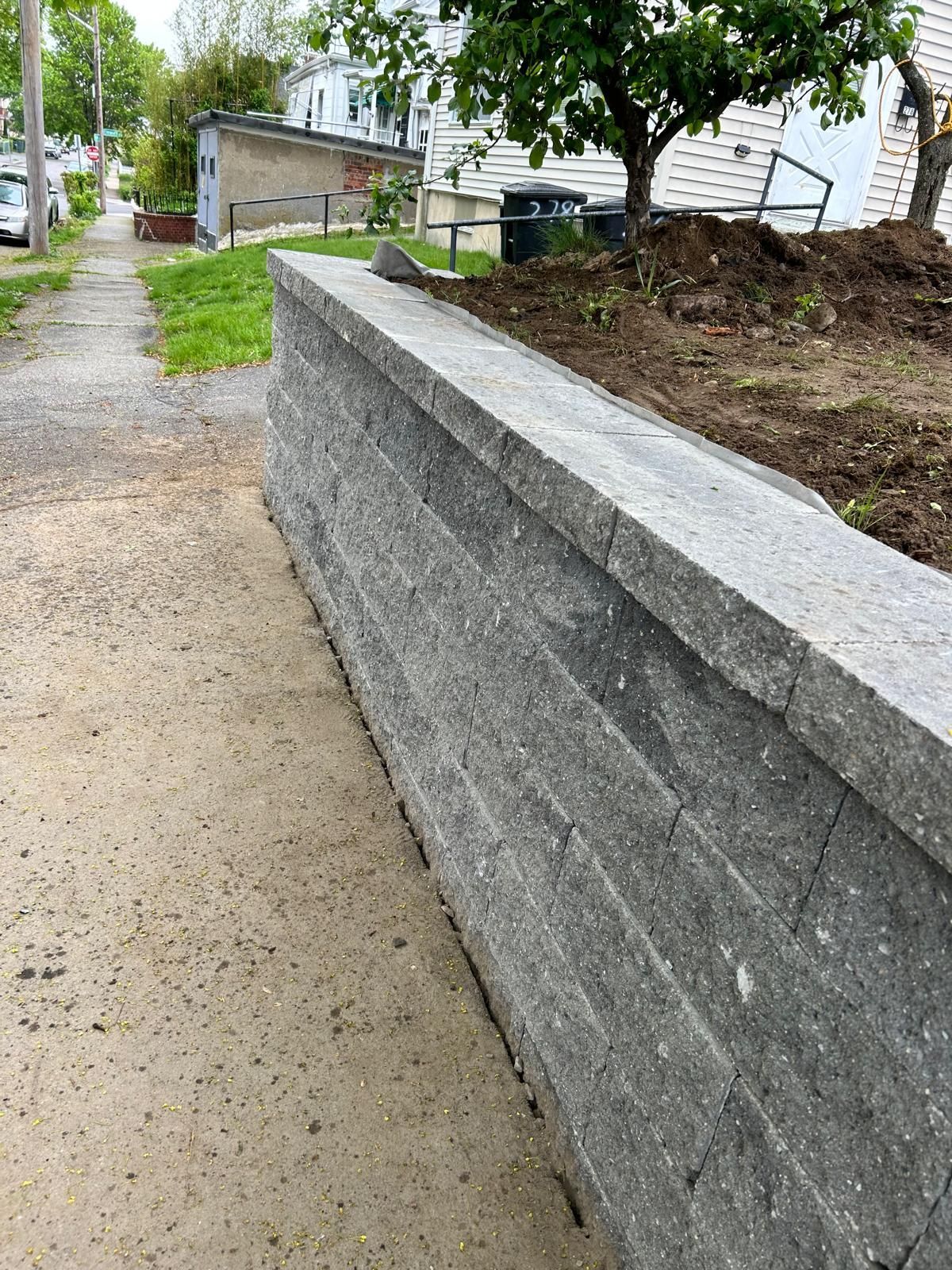 A gray retaining wall next to a sidewalk; dirt and grass in the background.