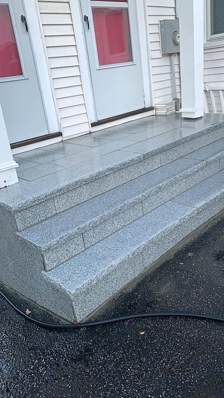Gray speckled stone steps leading up to white building with red-framed doors.