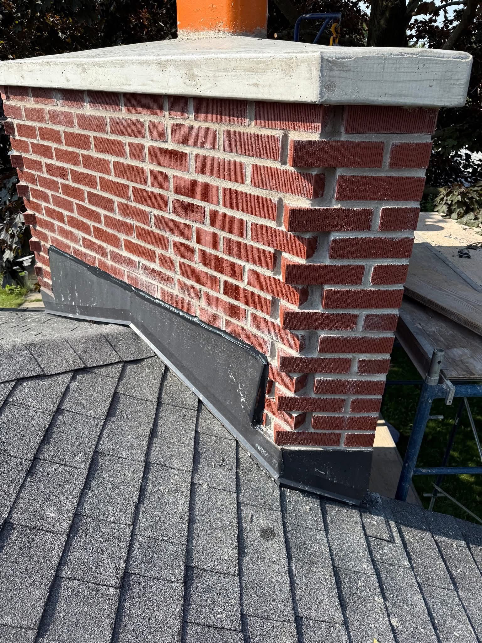 Brick chimney on a gray shingle roof with black flashing.