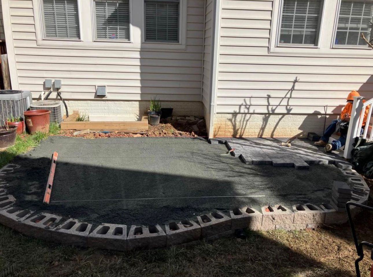 A patio under construction with pavers, gravel, and a retaining wall near a house.