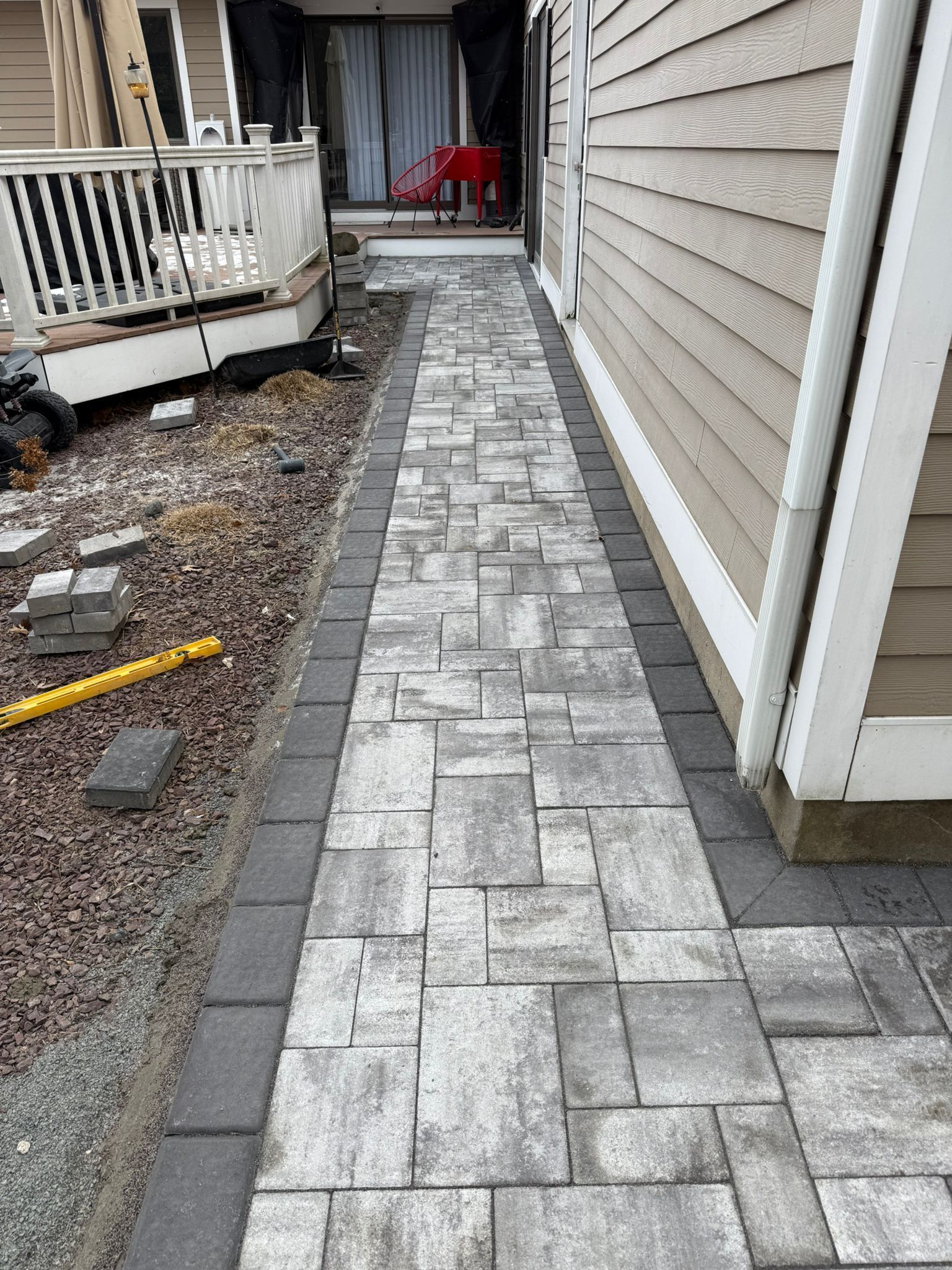Stone paver walkway between a building and a deck, with a border and brown gravel.