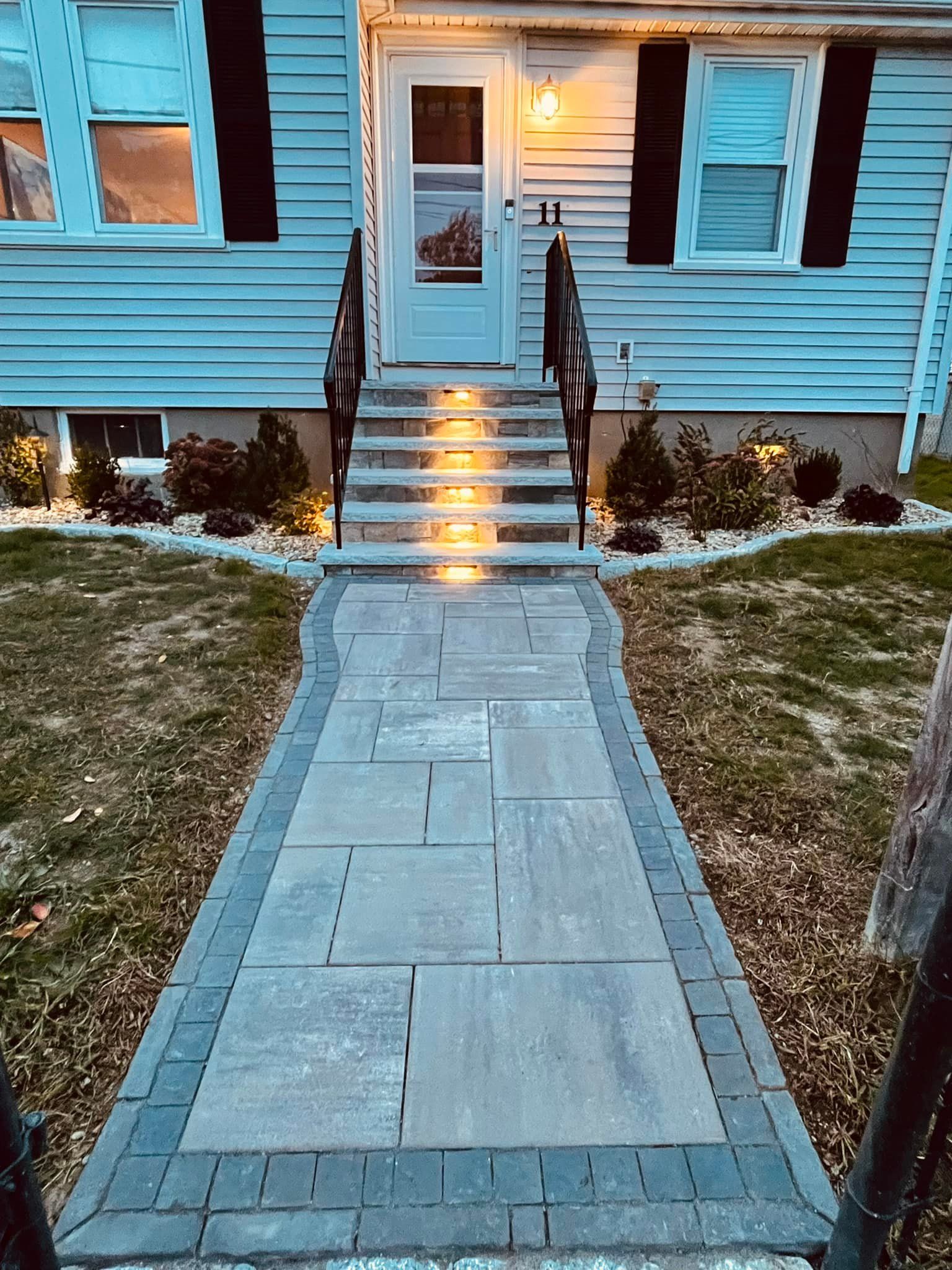 Stone walkway leading to a house with lit steps and entryway.