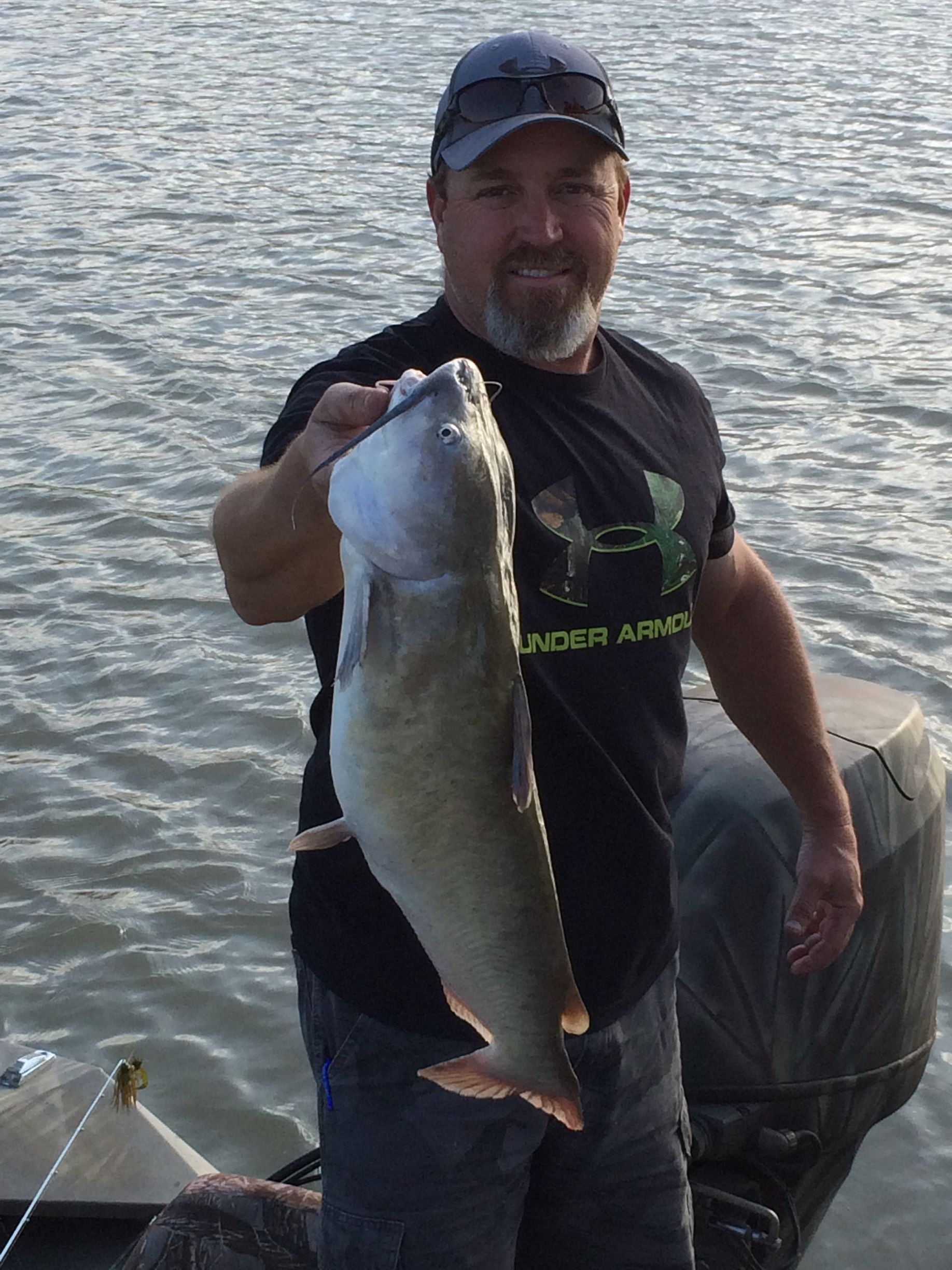 A man in an under armour shirt is holding a large fish