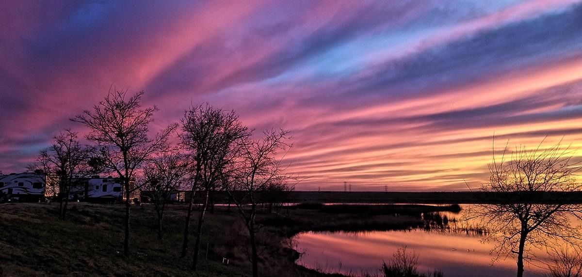 A sunset over a body of water with trees in the foreground and a bridge in the background