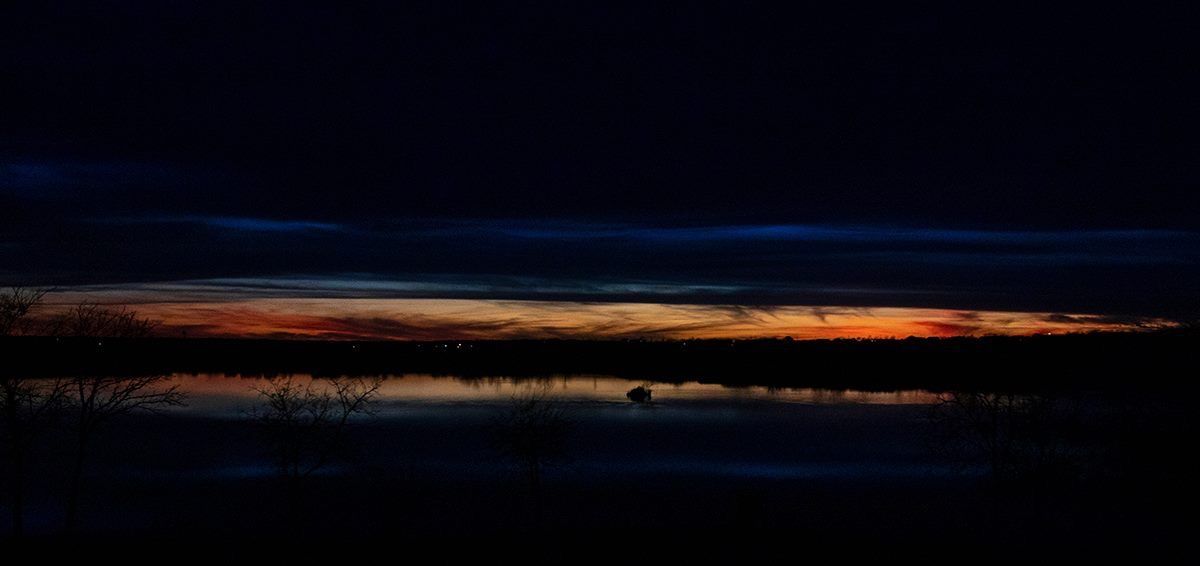 A sunset over a lake with a silhouette of a person in the water
