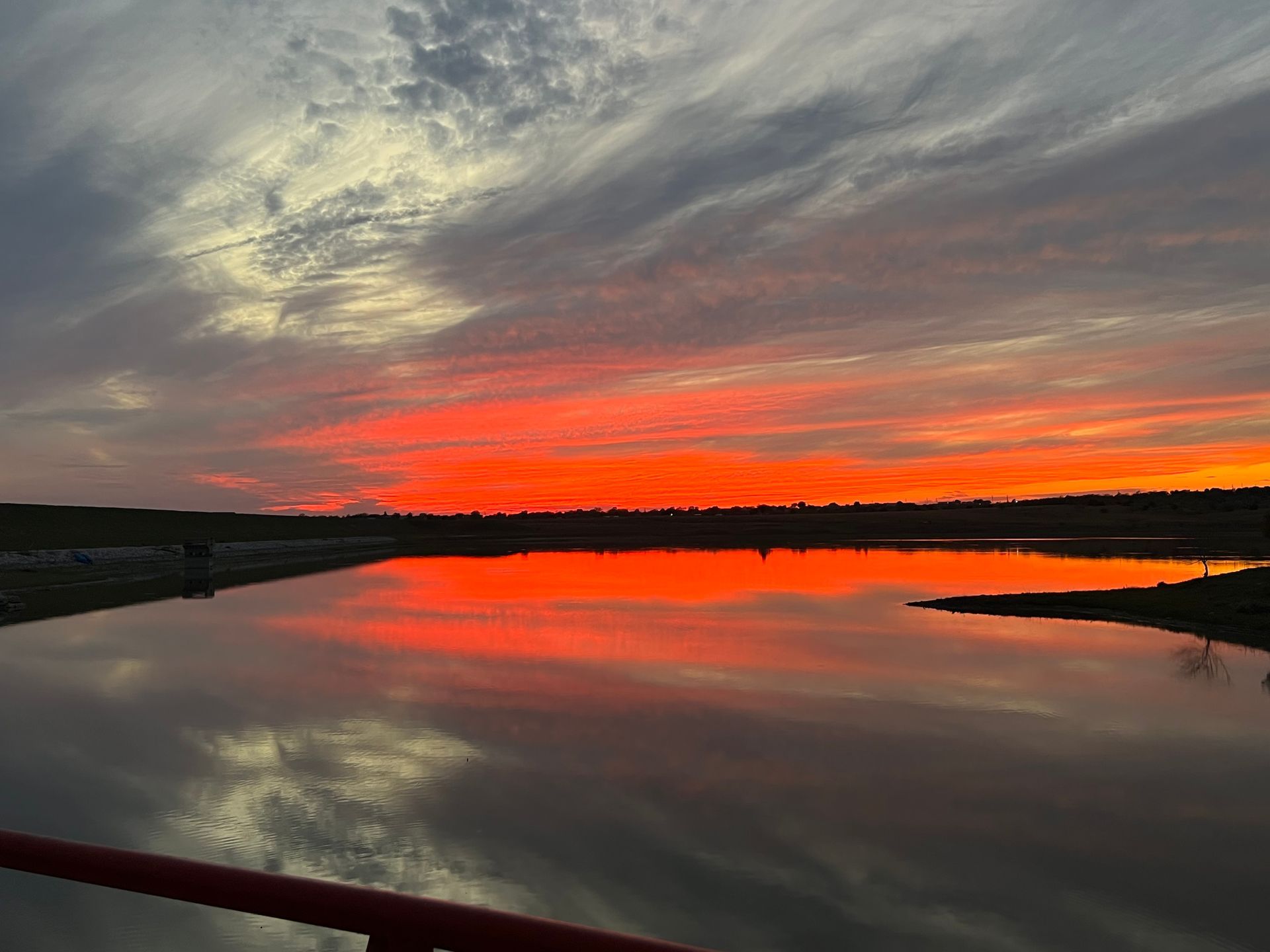 A sunset over a lake with a red sky and clouds reflected in the water