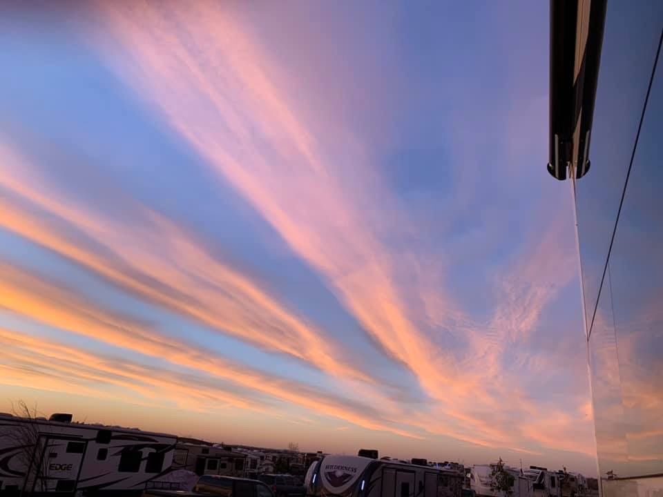 A sunset over an RV park with a lot of RVs parked in the background