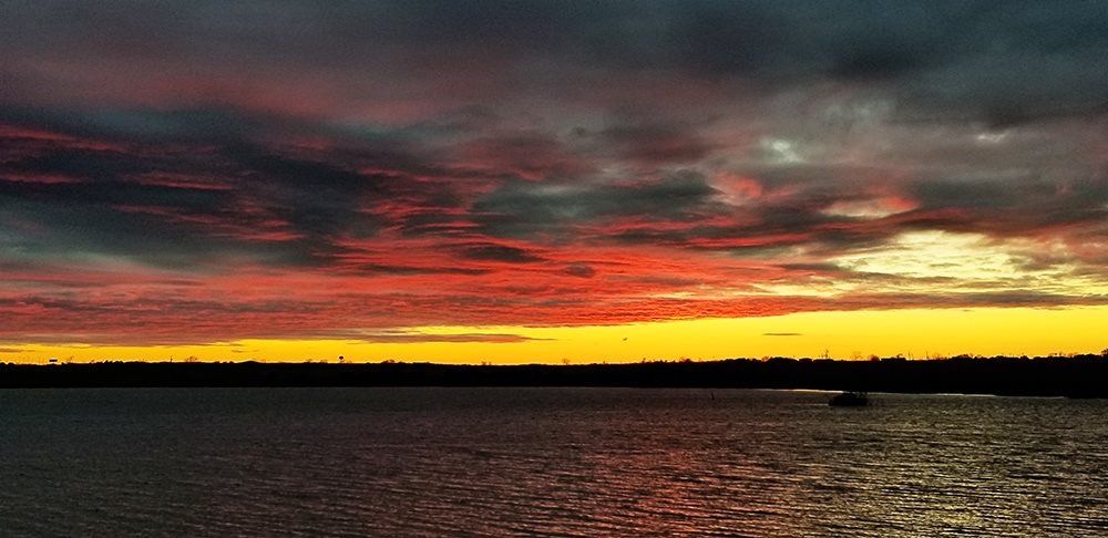 A sunset over a body of water with a boat in the distance