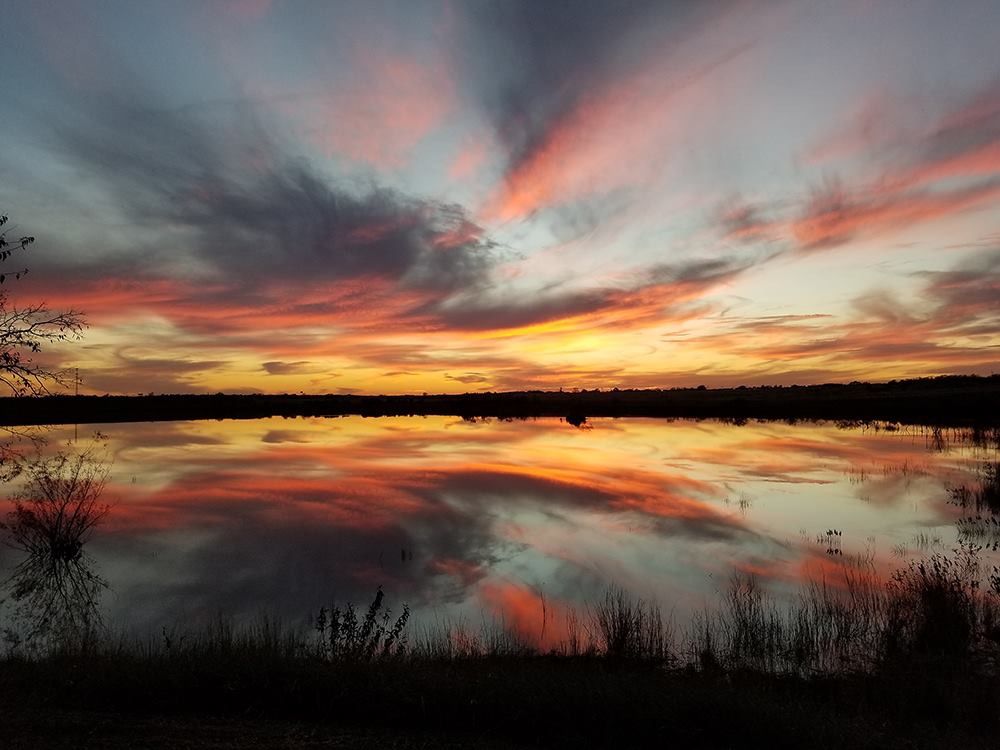 A sunset over a lake with a reflection of the sky in the water