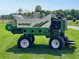 A green and white EarthTurf machine sits on a green grass field under a blue sky.