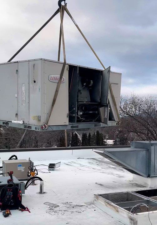 Commercial HVAC system being lifted by a crane on top of a snow covered roof