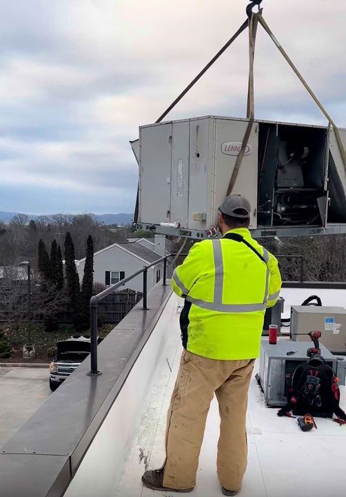A man in a yellow jacket assisting the carrying of a commercial HVAC system