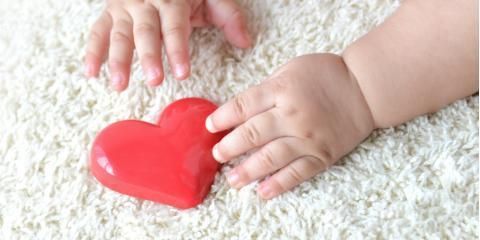 A baby 's hand is holding a red heart on a white carpet.