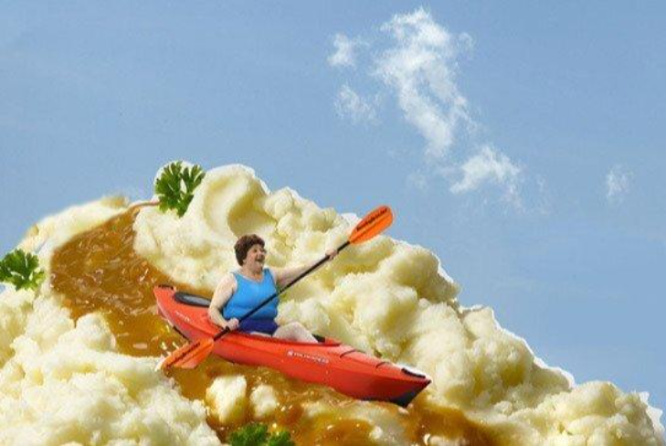 Woman kayaking through gravy on a mountain of mashed potatoes under a blue sky.